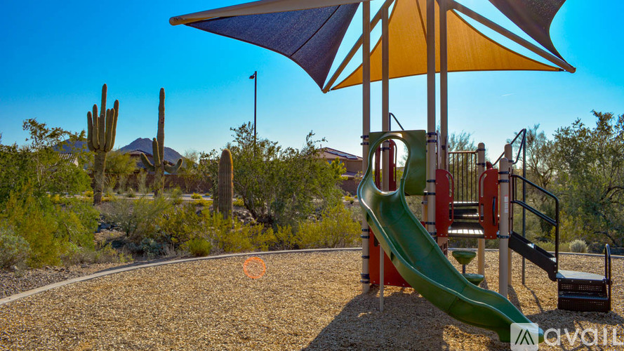 A playground with a green slide and a blue and yellow umbrella.