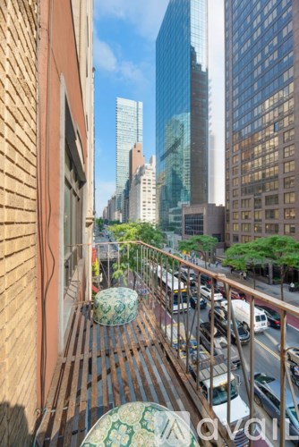 A balcony with a table and chairs overlooks a busy street with cars and tall buildings.