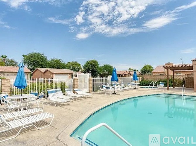 A pool with sun loungers and umbrellas in front of a fence and houses.