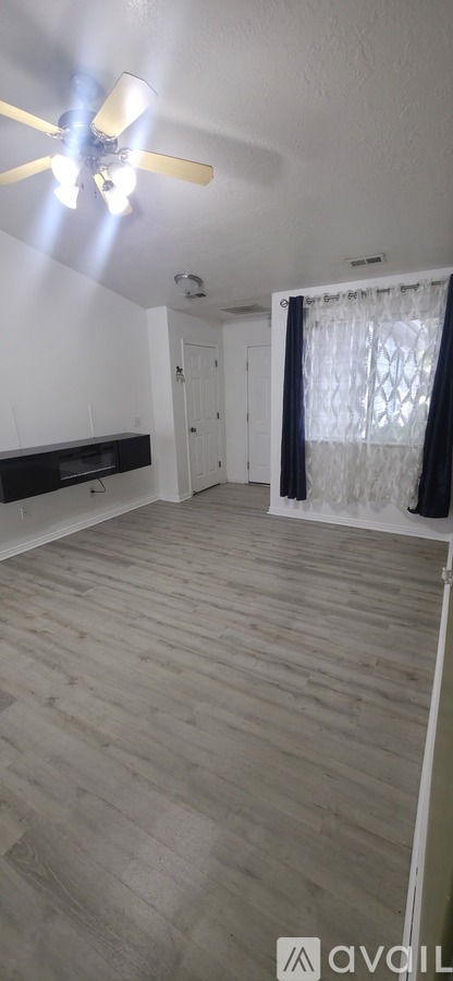 A room with a ceiling fan and a window with curtains.
