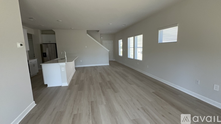 A spacious living room with light wood flooring and a staircase leading to another level.