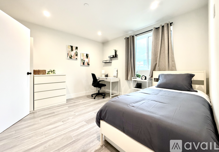A bedroom with a large bed, a desk with a chair, and a window with curtains.