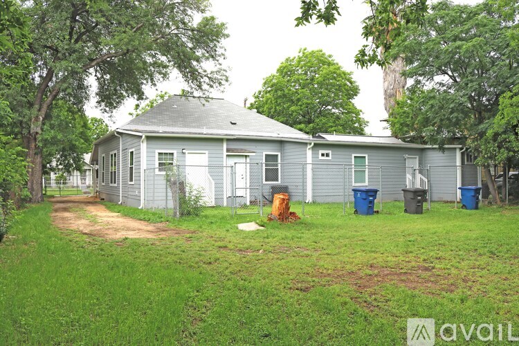 A house with a grey roof and a white door is surrounded by trees and has a dirt path leading to it.