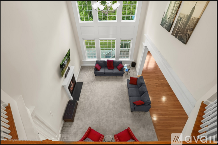 A living room with a grey rug and a grey couch with red pillows.