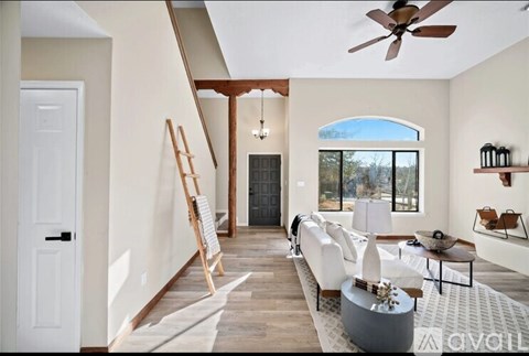 A modern living room with a white sofa set, a wooden floor, and a large window.