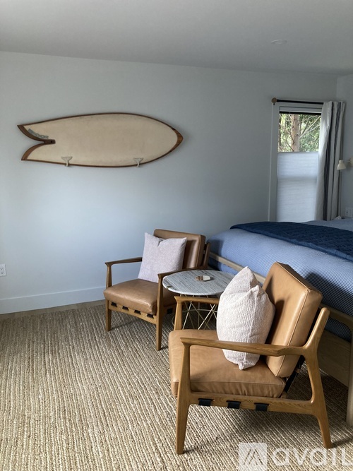 A bedroom with a bed, chair, and a surfboard on the wall.