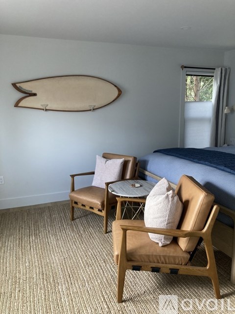 A bedroom with a bed, chair, and a surfboard on the wall.