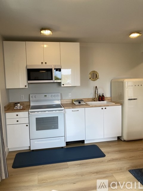 A kitchen with white cabinets and appliances, a blue mat on the floor, and a clock on the wall.