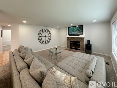 A living room with a large grey sofa and a clock on the wall.