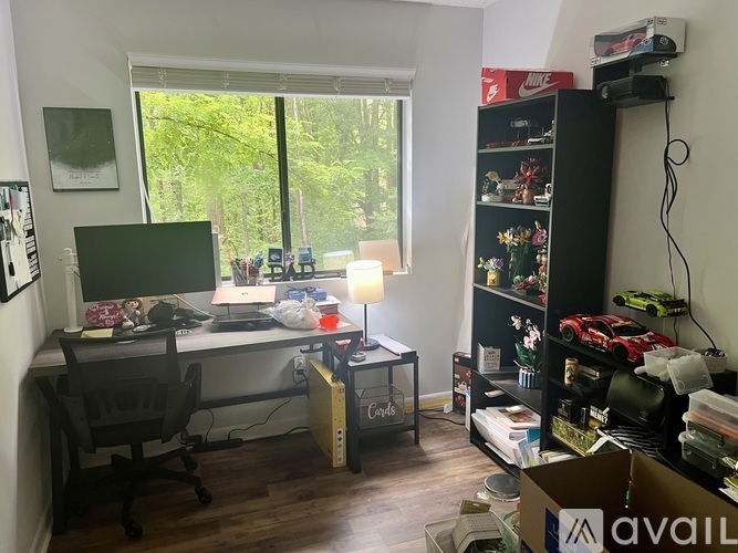 A room with a desk, computer, chair, and a window with a view of trees.