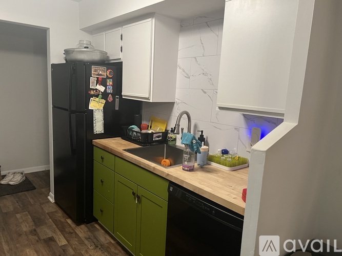 A kitchen with a black fridge and green cabinets.