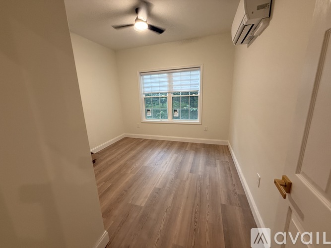 A room with a ceiling fan and a window overlooking a building.