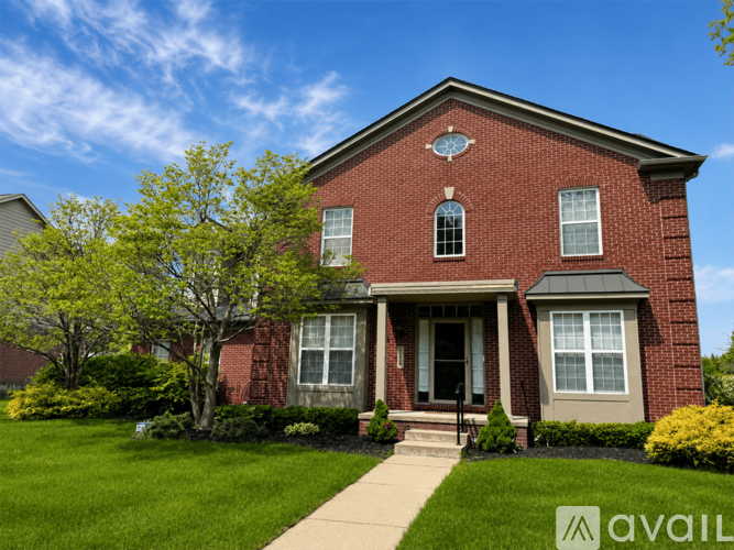 A red brick house with a front porch and a tree in front.