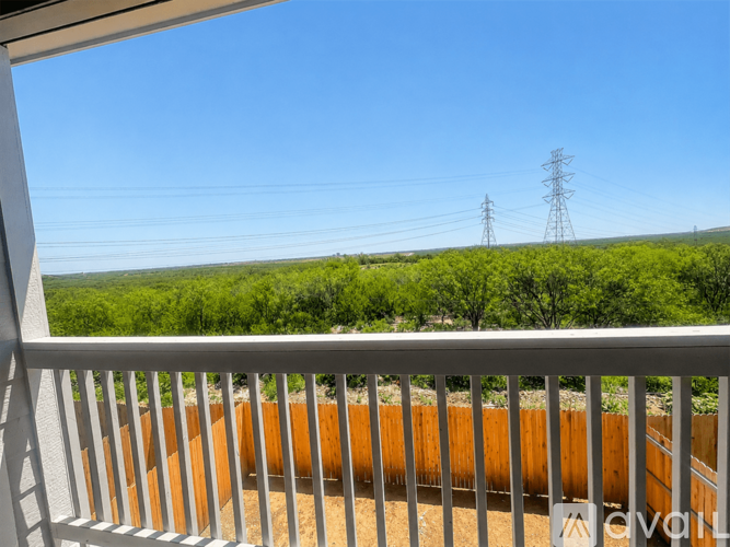 A balcony with a white railing overlooks a field with trees and power lines in the distance.