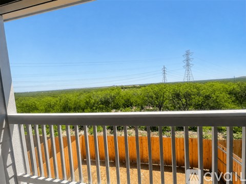 A balcony with a white railing overlooks a field with trees and power lines in the distance.