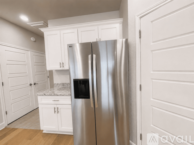 A stainless steel refrigerator stands in a kitchen with white cabinets.