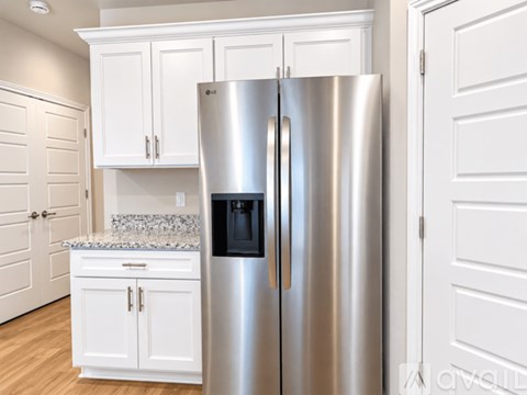 A stainless steel refrigerator stands in a kitchen with white cabinets.