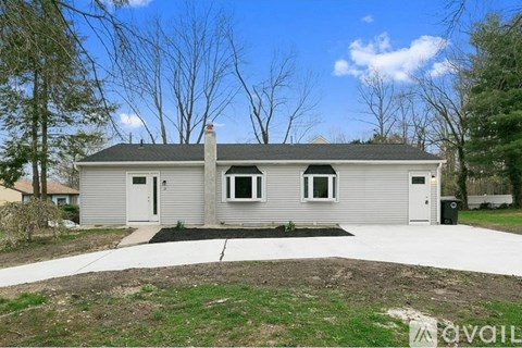 A grey house with a white door and windows is surrounded by trees and grass.