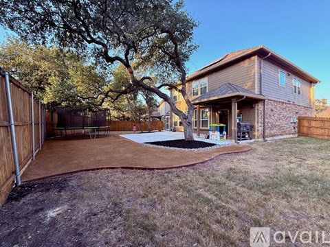 A backyard with a tree, a patio and a house.