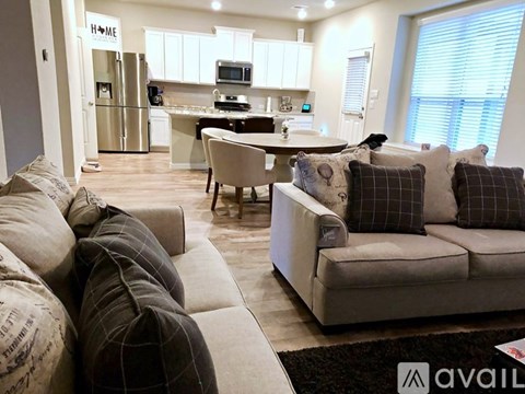 A living room with a couch, chair, and a kitchen area in the background.
