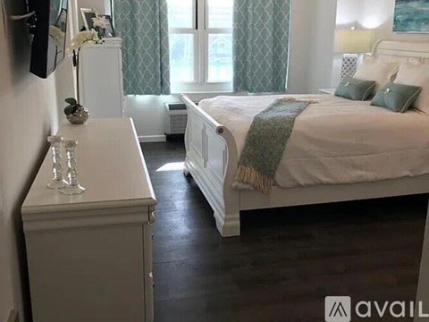 A white bedroom with a large bed and a nightstand with a vase on it.