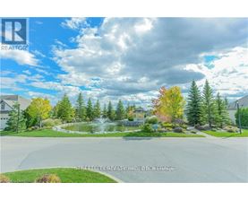 A real estate listing photo of a house with a pond and trees in the background.