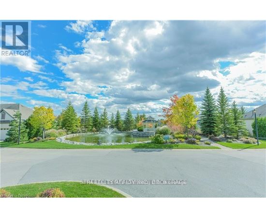 A real estate listing photo of a house with a pond and trees in the background.
