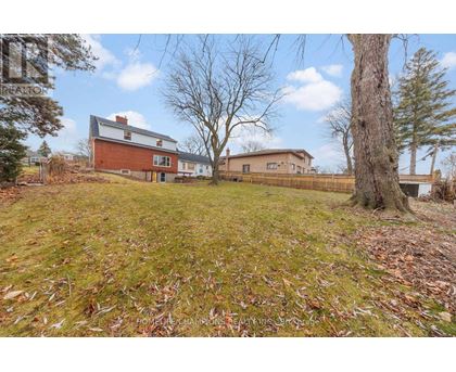 A house with a red brick chimney is surrounded by a grassy field with fallen leaves.