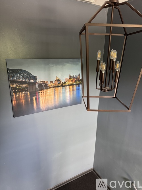 A modern chandelier hangs above a large framed picture of a bridge over a river.