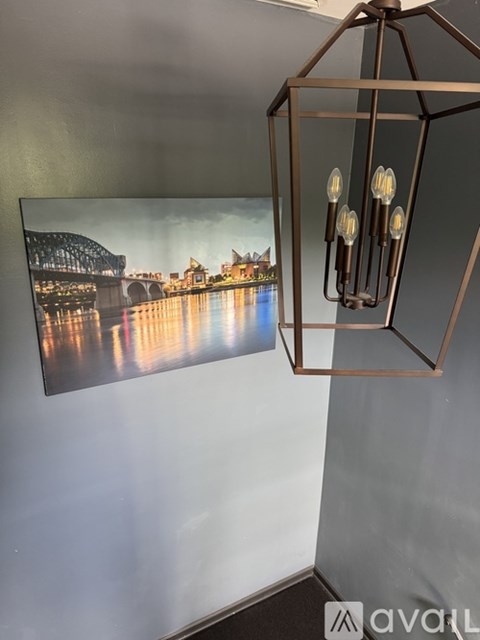 A modern chandelier hangs above a large framed picture of a bridge over a river.
