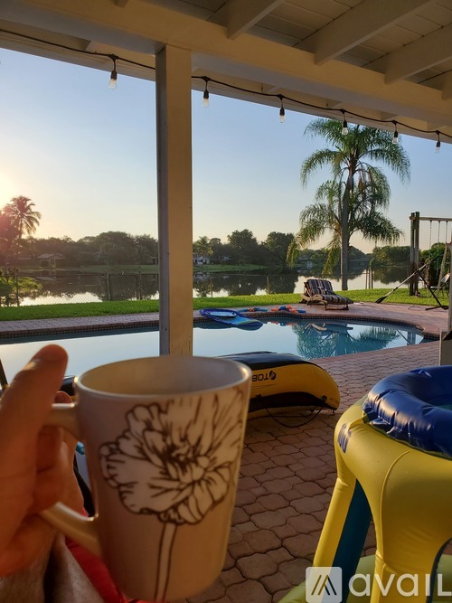 A person is holding a mug with a flower design in front of a pool area.