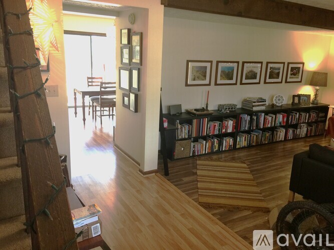 A living room with a staircase on the left and a bookshelf filled with books on the right.