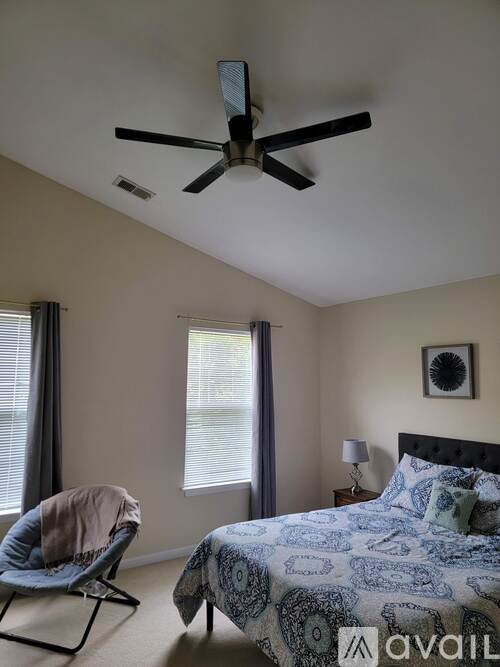 A bedroom with a bed, chair, and ceiling fan.
