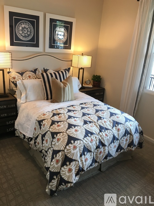 A bed with a white and blue comforter and pillows in a room with two wall lamps.