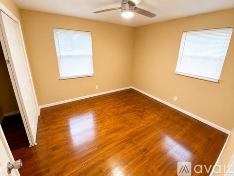 A room with wooden flooring and two windows.