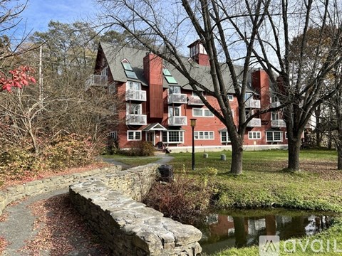 A red brick building with a stone wall and a pond in front.