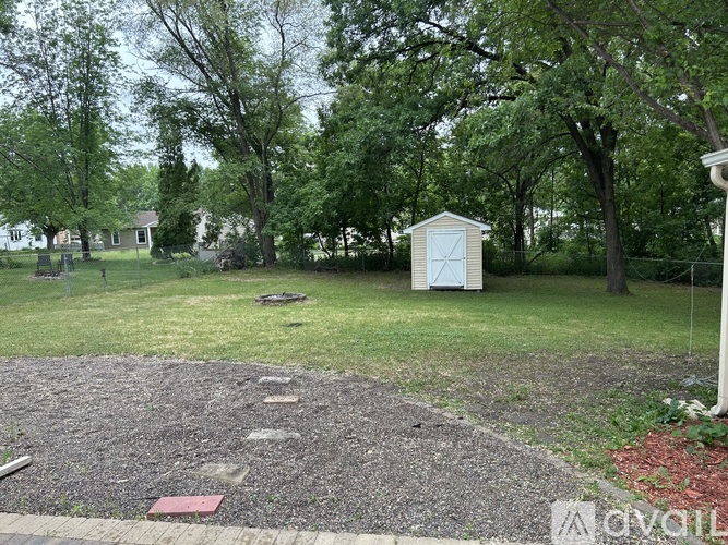A small white shed sits in a grassy area with a gravel path leading to it.