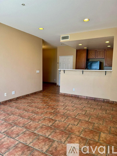 A room with tiled flooring and a kitchen area with cabinets and a refrigerator.