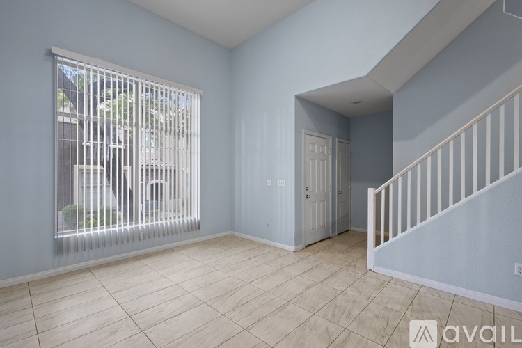 A room with a window covered by vertical blinds, a wooden staircase, and a door.
