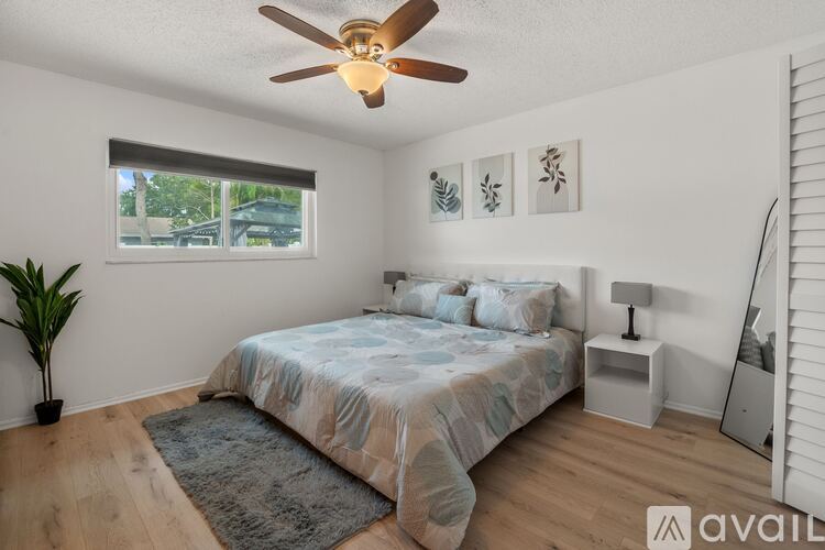 A bedroom with a bed, a ceiling fan, and a window with a view of a parking lot.
