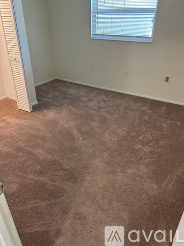 A room with a carpeted floor and a window with blinds.