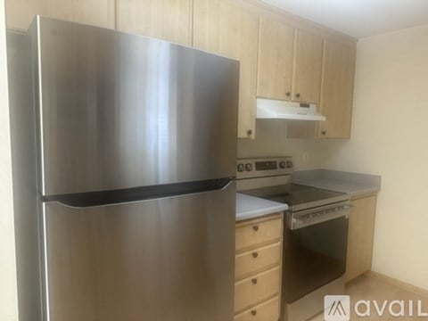 A stainless steel refrigerator stands in a kitchen with wooden cabinets and a stove top oven.