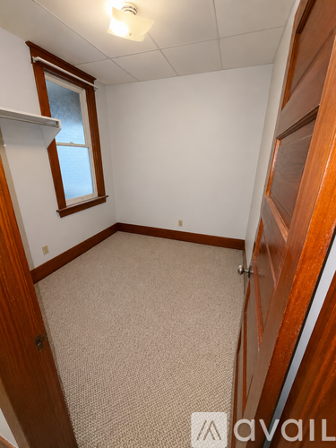 A small, empty room with a window and carpeted floor.