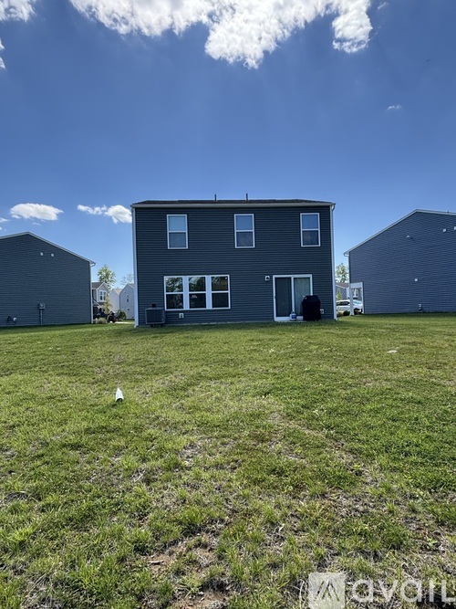 A grey house with a white door and windows is surrounded by a grassy field.