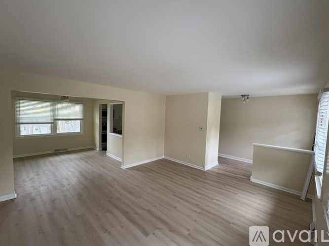 A spacious room with wooden flooring and a window with blinds.