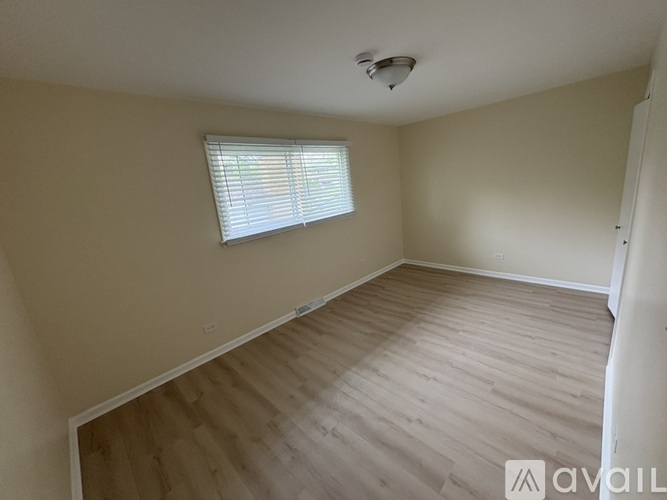 A room with wooden flooring and a window with blinds.