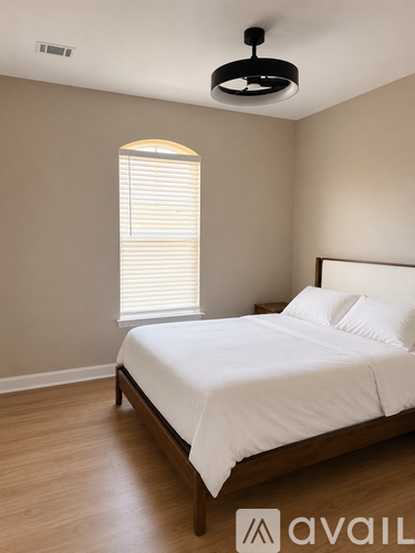 A bedroom with a bed, wooden floor, and a window with blinds.
