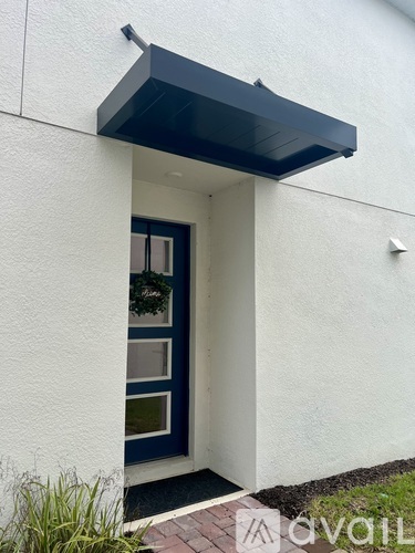 A white house with a black awning and a blue door.