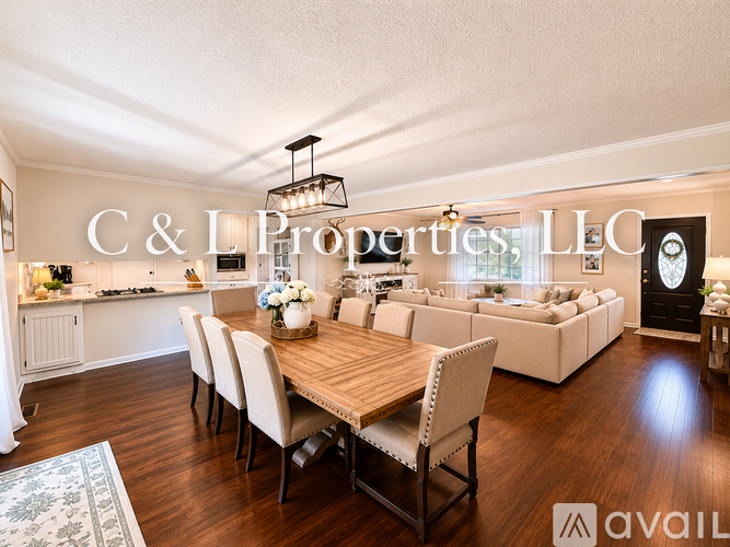 A well-lit, spacious living room with a dining table and chairs, and a kitchen area in the background.