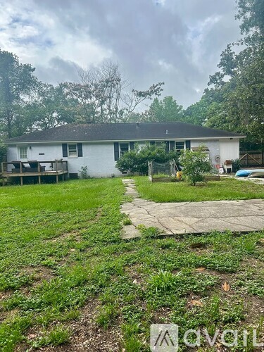 A house with a white exterior and a grey roof is surrounded by a grassy area and trees.
